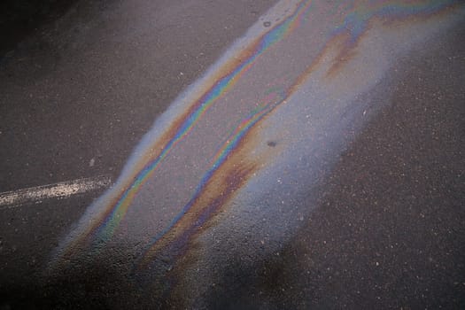 Colorful gasoline spill polluting wet asphalt road creating a rainbow effect.