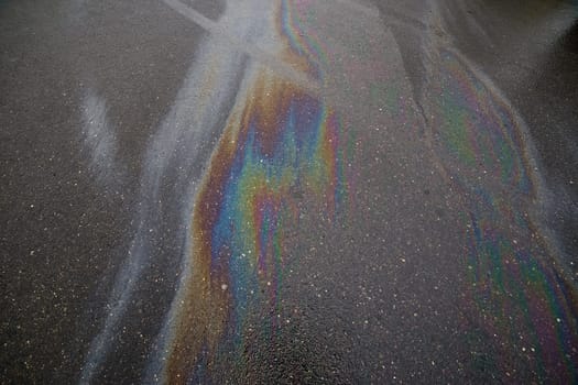 Gasoline rainbow on wet asphalt creates pollution.