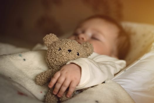 Sleeping newborn baby lying with a soft teddy bear under the blanket in warm, cozy sunlight. Childhood and parenting concept. High quality photo