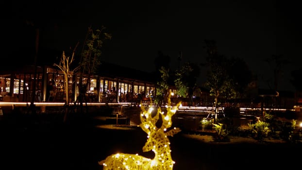Illuminated reindeer decoration with festive lights at night, outdoor setting with building in the background.