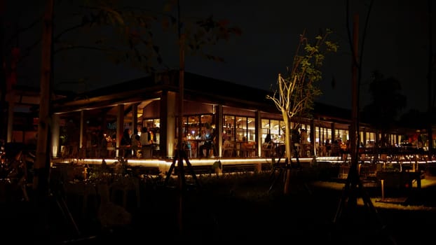 Cozy restaurant exterior at night with warm lighting and silhouettes of people dining inside.