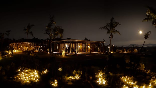 Tropical resort at night with illuminated bungalows and palm trees under moonlight.