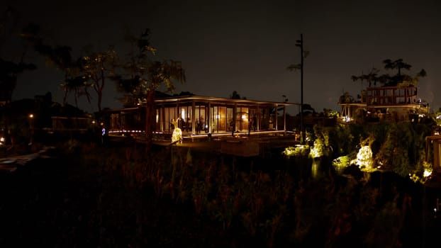 Tropical resort at night with illuminated bungalow and palm trees in the dark night