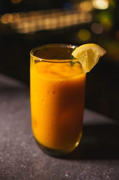 Refreshing mango smoothie in a glass with a lime slice, on a dark background.