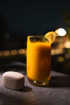Glass of fresh orange juice with a slice of lime, on a table at night. Bokeh lights in the background.