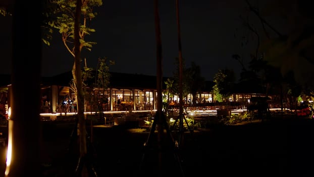 Nighttime view of a tranquil outdoor restaurant with ambient lighting and trees in the dark night