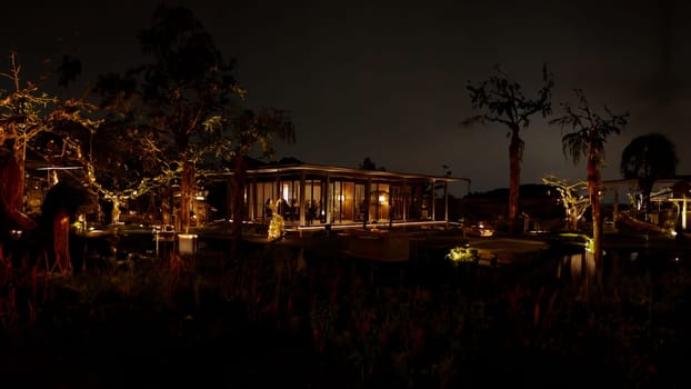 Luxurious house illuminated at night with warm lights, surrounded by trees and a calm water body, reflecting a serene ambiance in the dark night