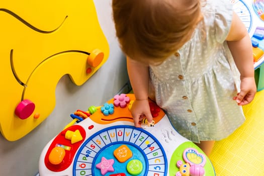 Toddler playing with an interactive toy designed for learning shapes and colors in a colorful playroom. Concept of combining fun and education to promote early development