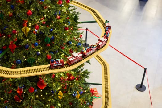 A vibrant and colorful train set is beautifully circling around a splendidly decorated Christmas tree, creating joy