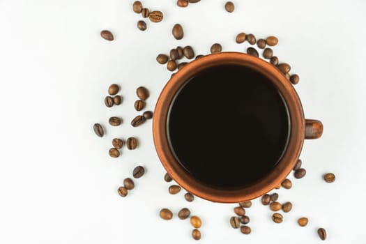 Overhead view of a ceramic coffee cup filled with black coffee surrounded by scattered roasted coffee beans on a clean white background.