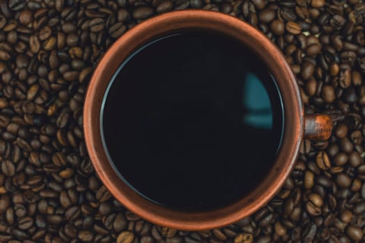A clay cup filled with black coffee placed on a bed of roasted coffee beans, viewed from above, creating a rustic and warm composition, no people.