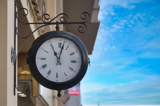 An elegant vintage clock beautifully hanging outdoors against a backdrop of a clear blue sky