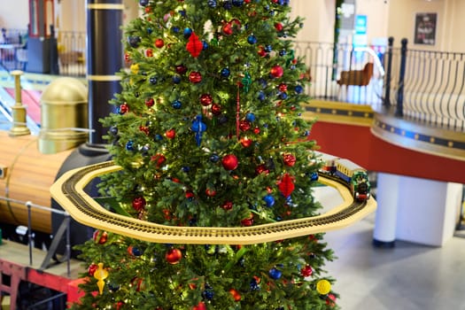 A beautifully and festively decorated Christmas tree featuring a charming model train circling around it joyfully