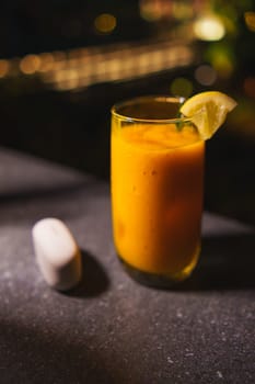Glass of fresh mango juice with a lime wedge on a dark bar counter, moody lighting, with bokeh background in the dark night
