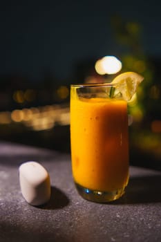 Refreshing mango smoothie with a lime garnish in a tall glass, served on a dark bar counter with bokeh lights in the background.
