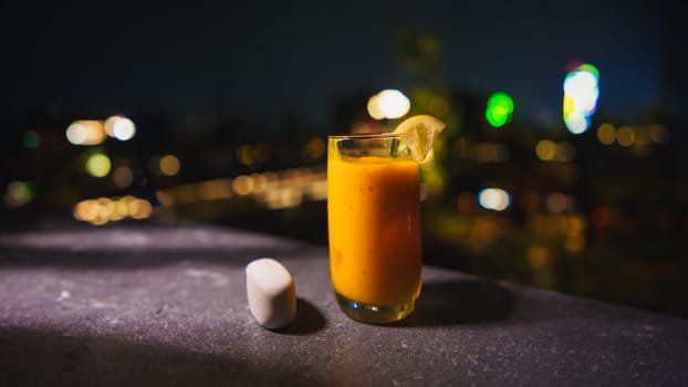 Glass of orange juice with a slice of lemon on a city night background.