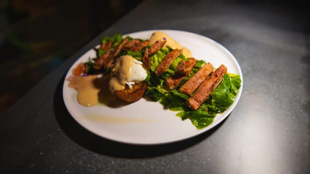 Gourmet meal with grilled meat, sauce, and greens on a white plate, spotlighted on a dark background in the cafe