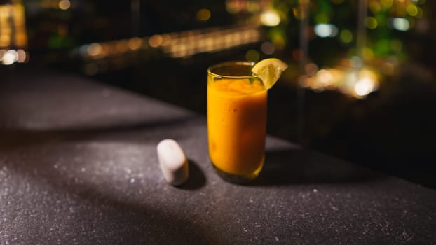 Refreshing orange cocktail with a lemon garnish on a dark bar counter, with blurred background lights in the dark night