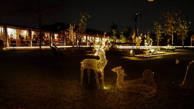 Illuminated reindeer light decorations at a festive outdoor setting at night with a blurred background of a restaurant in the dark night