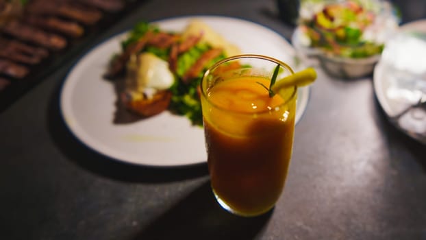 Iced tea in a glass with a straw, accompanied by a sandwich on a plate, served on a dark table in the night