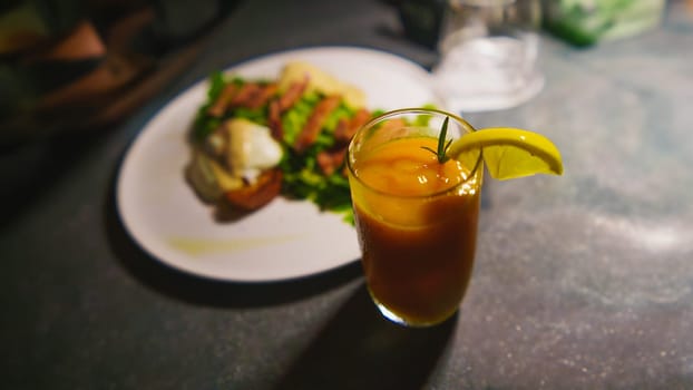 a glass of orange juice next to a plate of chicken meat and green salad on the table in the cafe at night