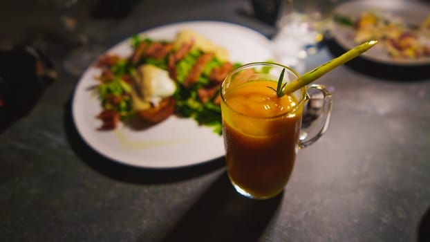 Glass of iced tea with straw, next to a plate of food on a dark table in the cafe