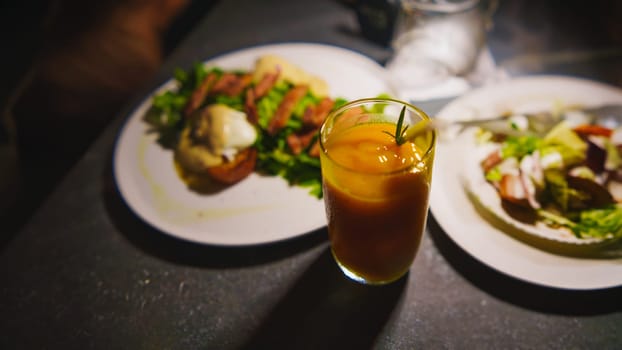 Elegant dining setting with a glass of orange drink and gourmet dishes in a dimly lit ambiance in the night