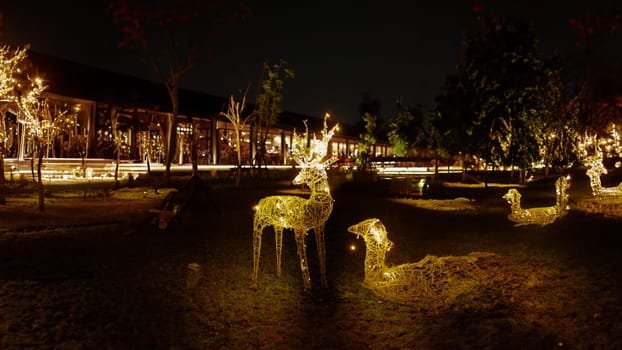 Illuminated reindeer Christmas decoration at night with ambient building lights in the background.
