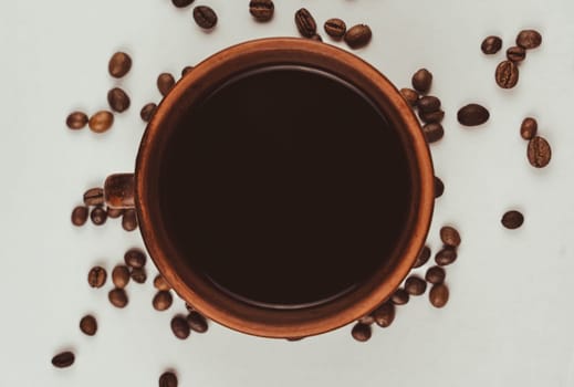 Ceramic coffee cup filled with black coffee, surrounded by scattered roasted coffee beans on a clean white background in an overhead composition.