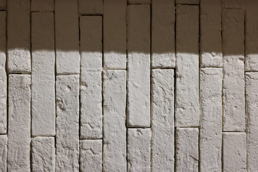 A closeup image of a textured white wall showcasing uneven brick patterns and soft, artistic shadows