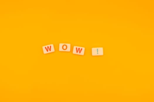 Close-up of Scrabble tiles spelling WOW arranged on a vibrant yellow background, minimalistic style with copy space for creative designs.