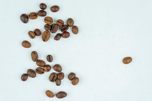 A scattered group of roasted coffee beans placed randomly on a clean white background, showcasing a minimalistic and natural arrangement.