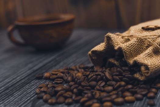 Rustic burlap sack spilling roasted coffee beans onto a dark wooden surface, with a blurred ceramic coffee cup in the background, creating a cozy atmosphere.