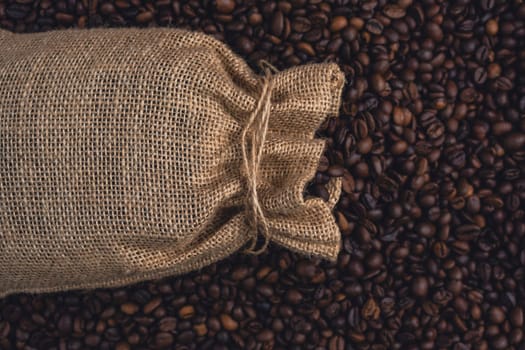 A burlap sack tied with string lying on a bed of roasted coffee beans, representing coffee storage, trade, or rustic aesthetics.