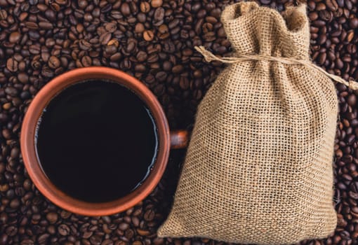 Overhead view of a cup of black coffee and a burlap sack placed on a bed of roasted coffee beans, creating a rustic coffee concept.