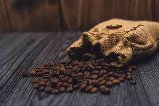 A rustic burlap sack spilling roasted coffee beans onto a textured dark wooden surface, creating a cozy and natural still-life composition.