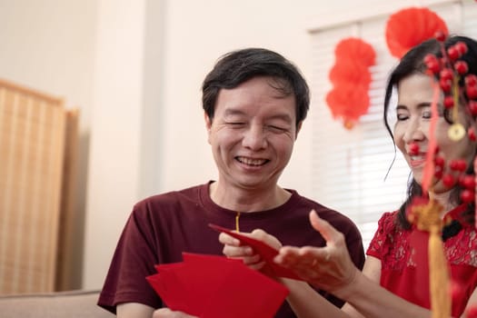 An elderly couple enjoys the warmth of Chinese New Year sharing traditional red envelopes and celebrating together in a cozy home.
