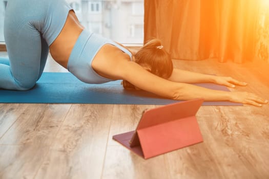 Young athletic attractive woman practicing yoga doing exercises. Works out at home or in a yoga studio, sportswear, blue pants and a full-length top indoors. Healthy lifestyle concept.