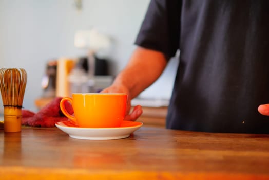 A skilled barista carefully serves a vibrant and eyecatching orange cup on a rustic wooden surface