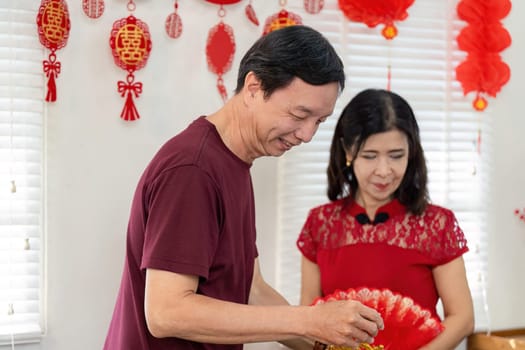 An elderly Chinese couple joyfully prepares for Chinese New Year surrounded by festive decorations and warm memories.