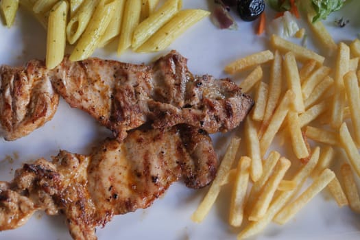 A truly delicious and appetizing plate featuring perfectly grilled chicken, pasta, and crispy fries