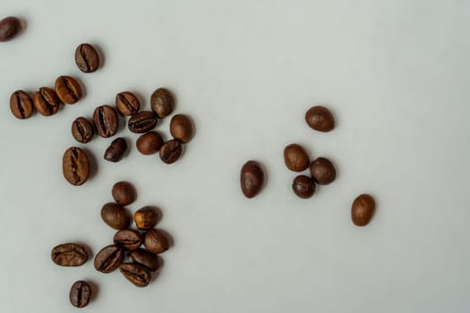 Close-up view of roasted coffee beans scattered and grouped unevenly on a clean white background, creating a minimalistic and natural look.