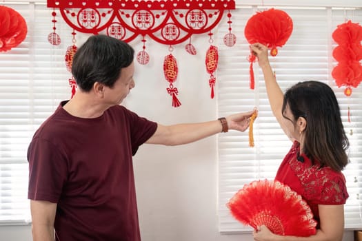An elderly Chinese couple joyfully celebrates Chinese New Year at home surrounded by festive decorations and traditions.