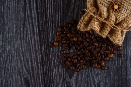 A burlap sack spilling roasted coffee beans onto a textured dark wooden surface, creating a rustic and natural aesthetic.