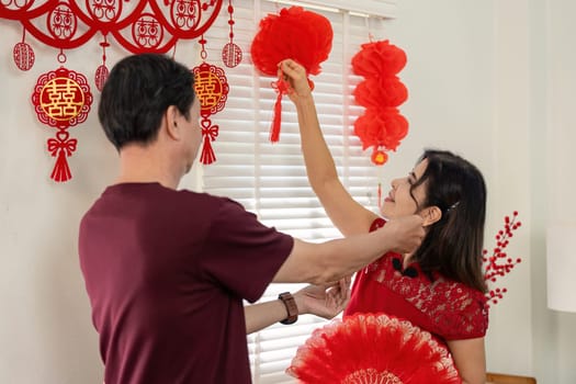 An elderly Chinese couple joyfully prepares for Chinese New Year surrounded by festive decorations and shared love.