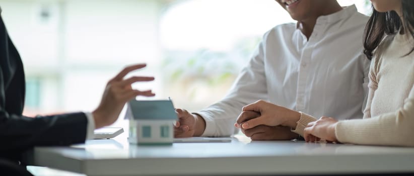 Young Asian couple making contract with house sale agency. man and his wife sitting signing the contract next to him looking the contract document with smile. real estate agreement successful concept.