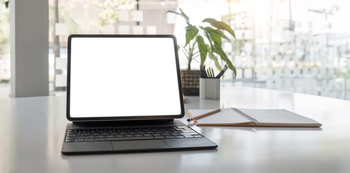 laptop white screen mockup, painting tools, notebook, and decor on a table in a modern contemporary living room. close-up workspace..