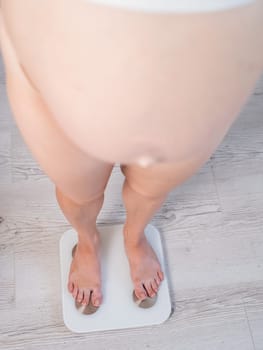 Top view of a pregnant woman with a bare tummy standing on an electronic scale