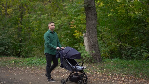 A young father walks through the forest with a sleeping child in a stroller. A man walks in an autumn park. 4k