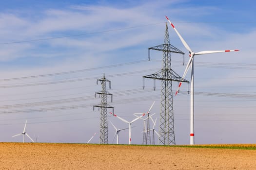 Field with many wind turbines of a wind turbine and power lines of several power poles under blue sky